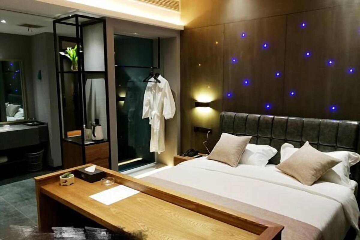 Moderni hotellihuone, jossa on suuri sänky, puinen yöpöytä, peili, vaatekaappi ja sinisillä valoilla varustettu seinä.