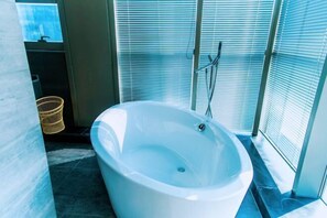 Un baño moderno con una bañera independiente, una cesta de mimbre y un ventanal con persianas.