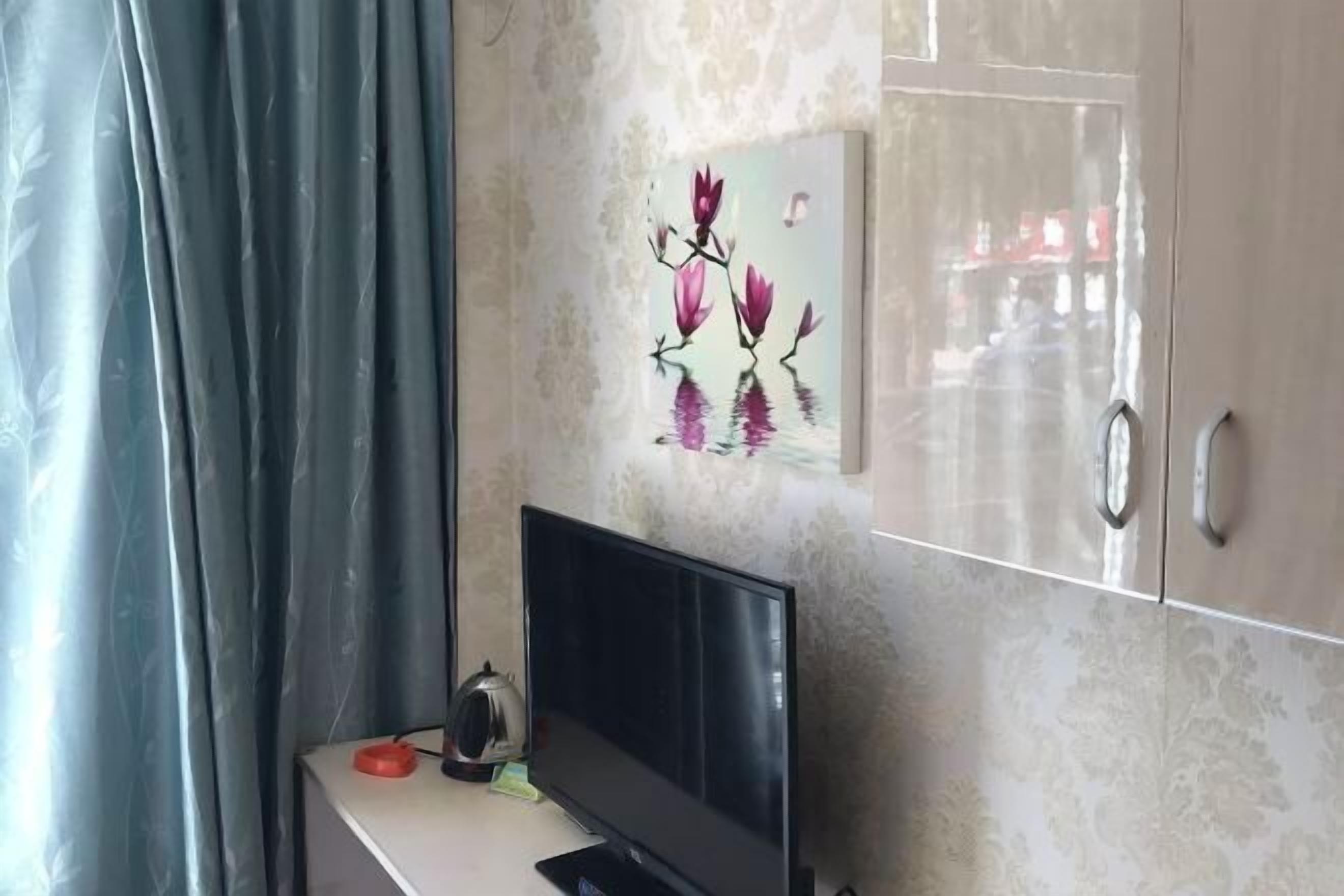 A room with a TV on a stand, a cabinet with a mirror, and a floral artwork on the wall.