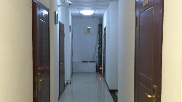 A narrow hallway with wooden doors on both sides, a tiled floor, and a ceiling with fluorescent lighting. - Hengchang Hotel (Shenyang)