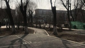 A park with a paved path, trees, and a building in the background. - Hengchang Hotel (Shenyang)