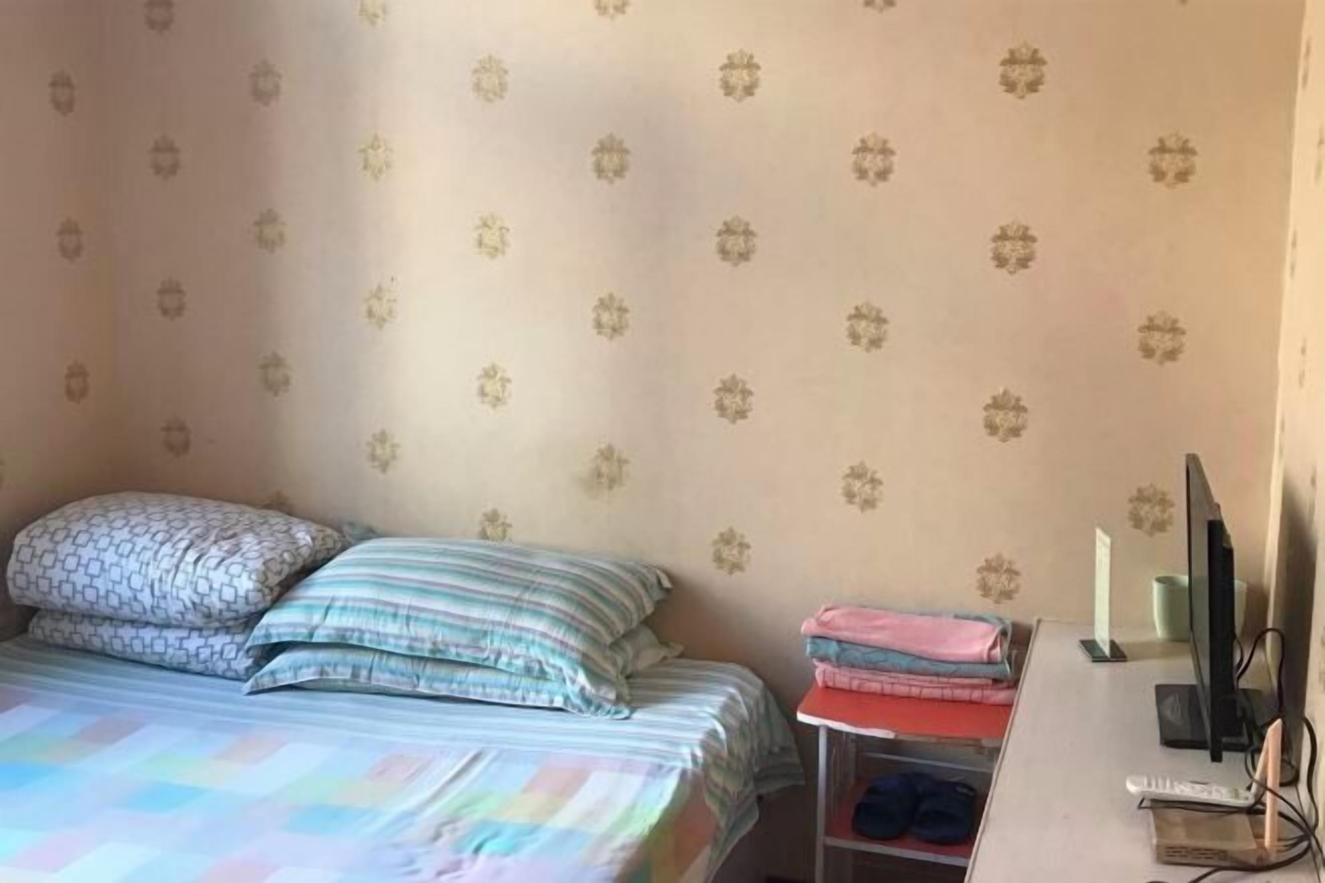 A bedroom with a bed, pillows, a desk with a computer, and a chair.
