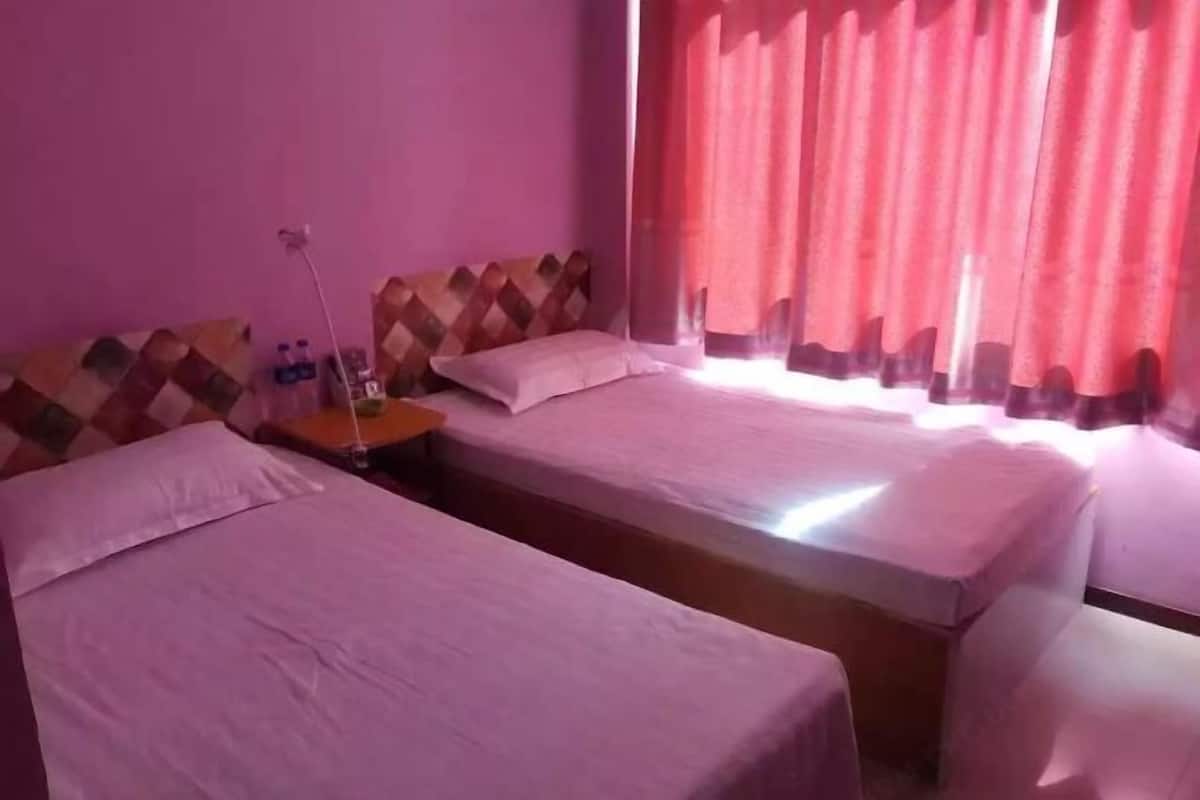 A room with two beds, a nightstand, and a window with red curtains.