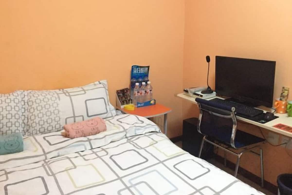 A hotel room with a bed, a desk with a computer, a chair, and a small table with a water bottle.