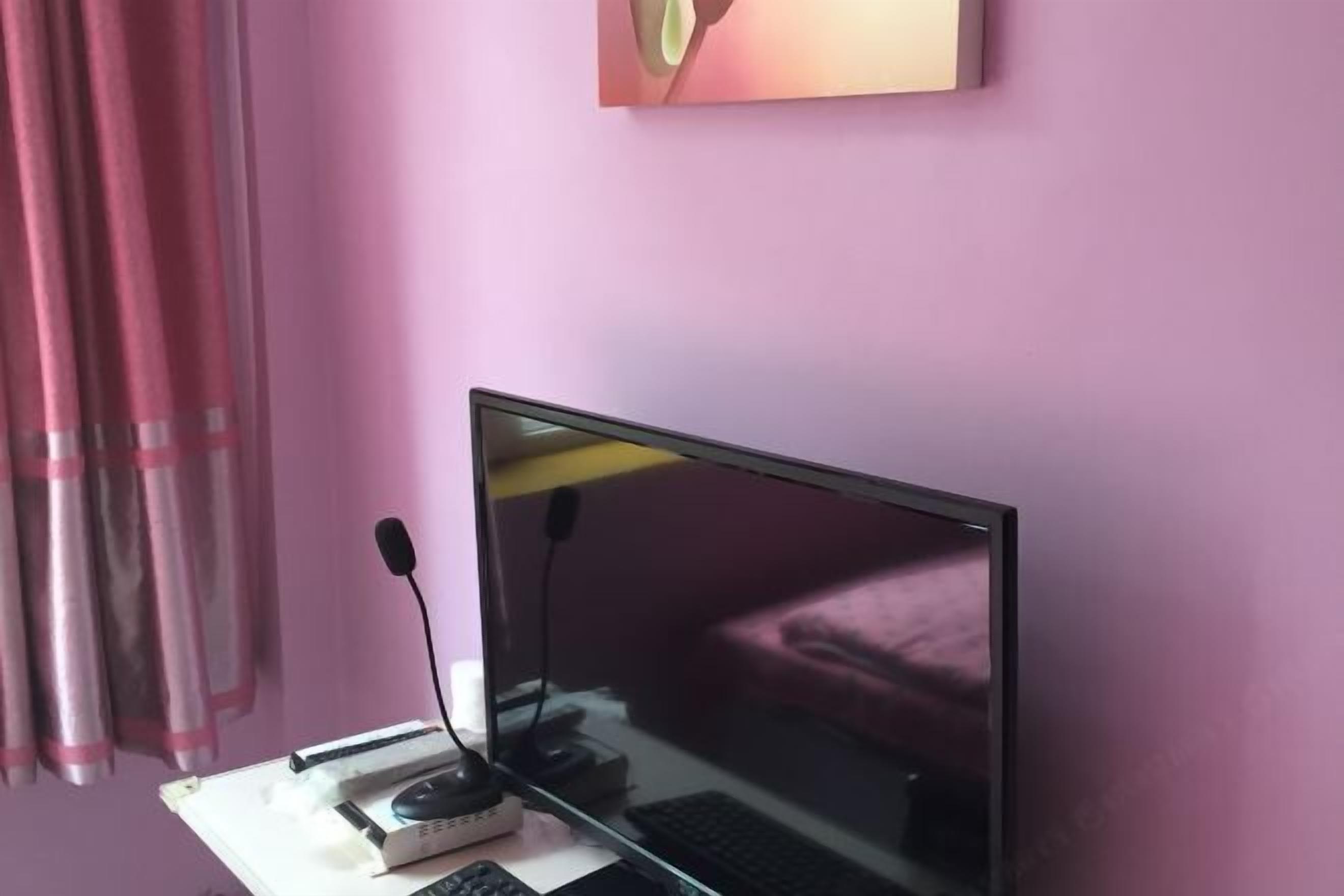A room with a bed, a desk with a computer, and a pink wall.