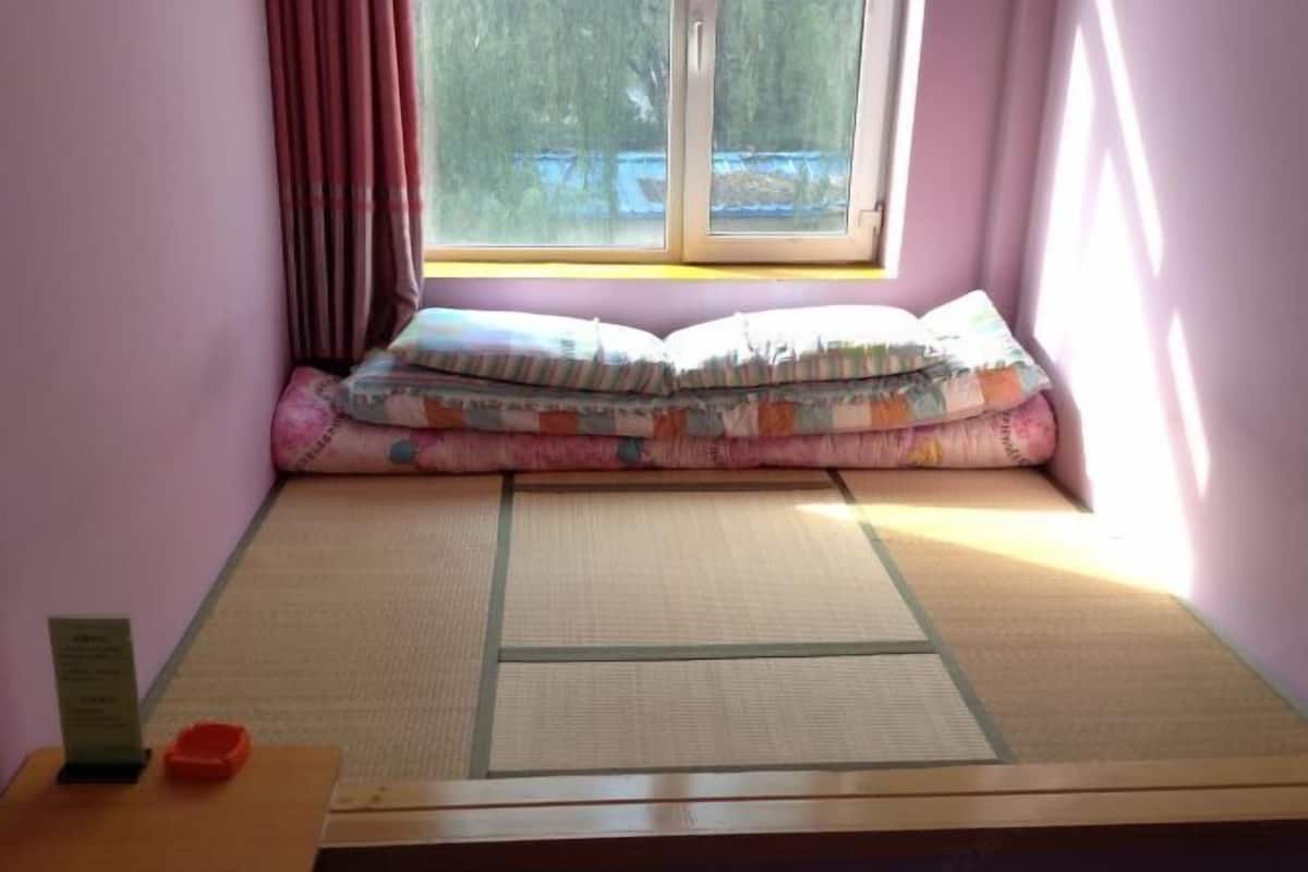 A tatami mat room with a futon bed, a small table with an orange object, and a window with curtains.