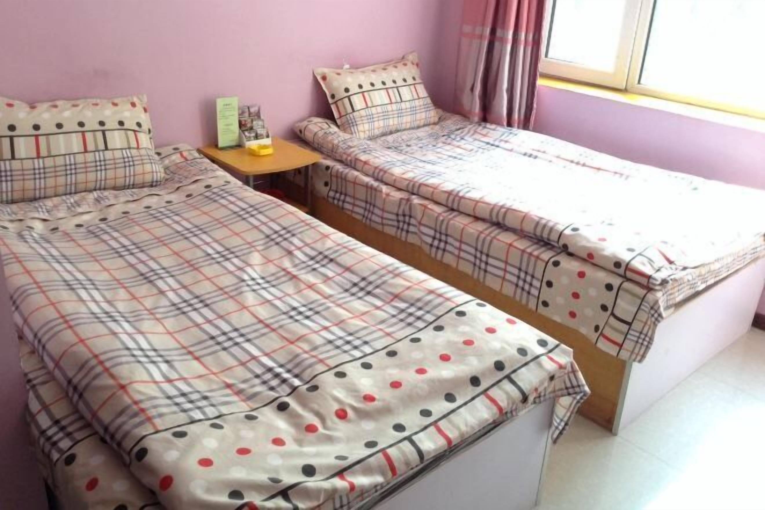 A room with two beds, a small table, and a window with curtains.