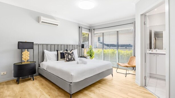 Ein modernes Schlafzimmer mit einem grauen Bett, einem schwarzen Nachttisch und einem Fenster mit Jalousien.