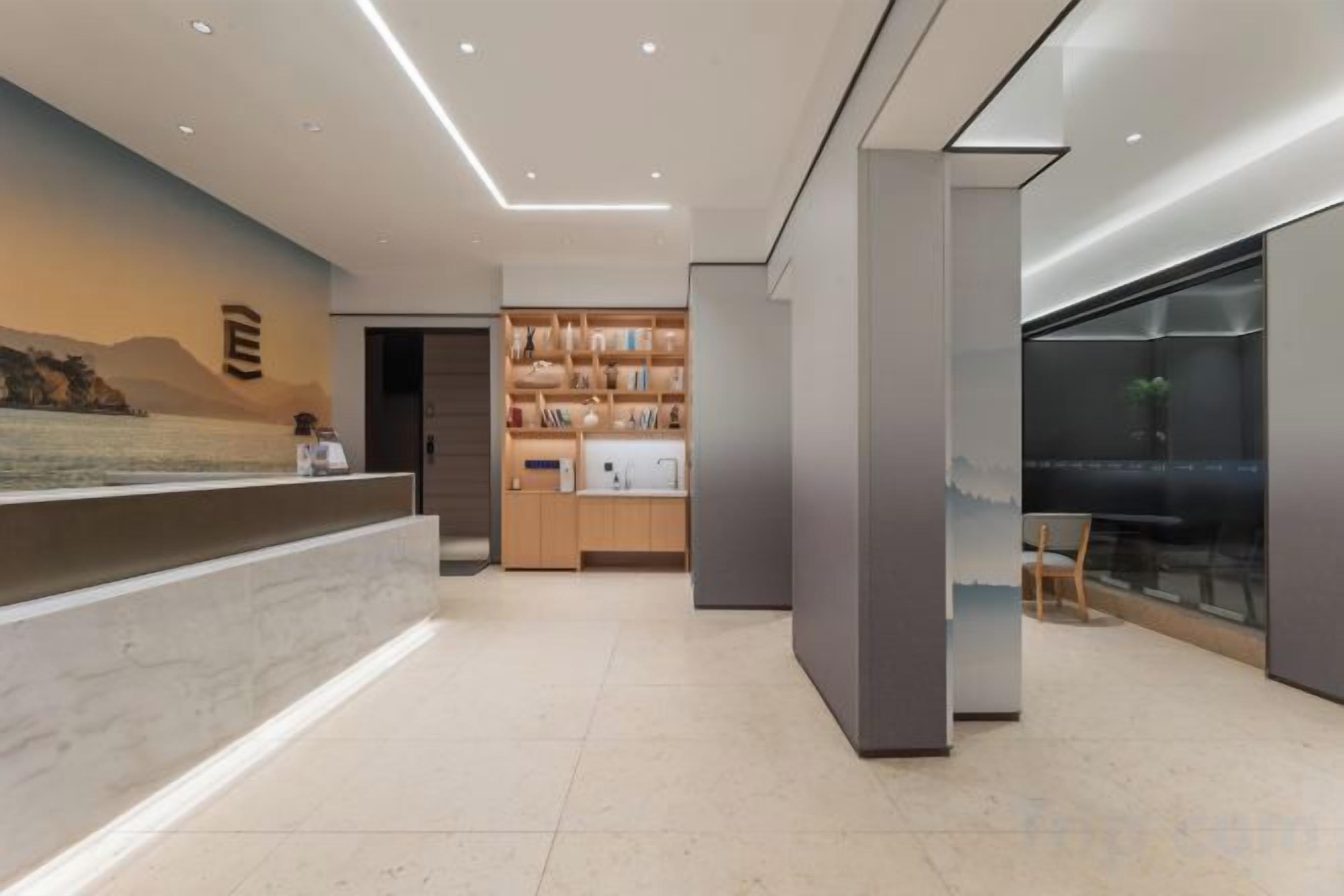A modern hotel lobby with a reception desk, a seating area, and a view of the outdoors.