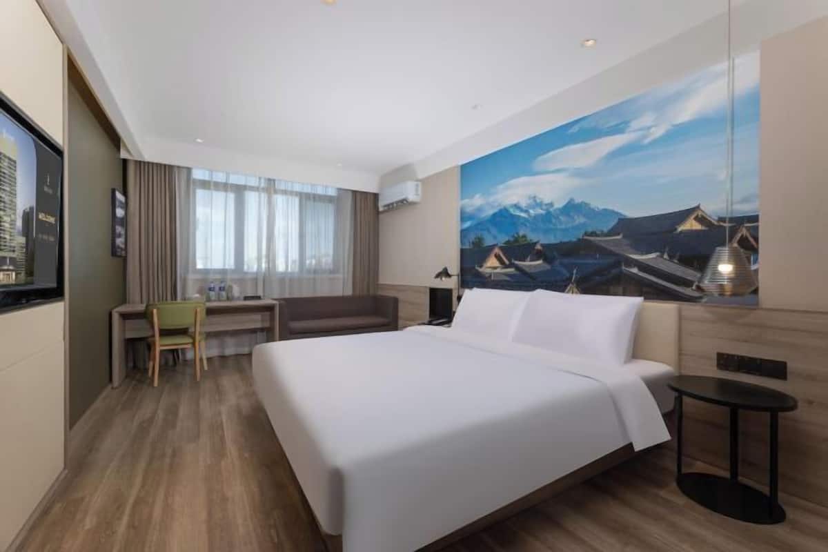 A hotel room with a bed, a desk, a chair, and a view of mountains through a window.