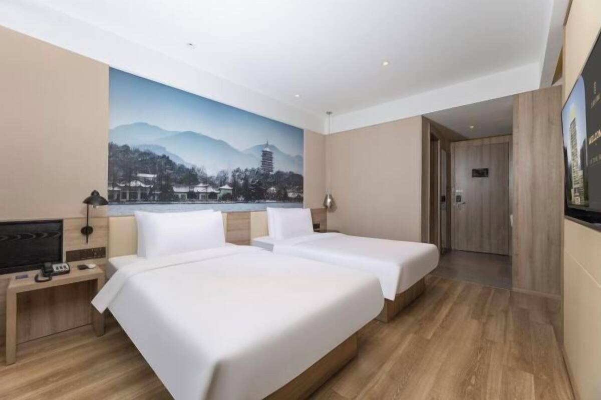 A hotel room with two beds, a desk with a TV, and a large mural of a mountain landscape.