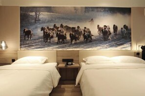Une chambre d’hôtel avec deux lits, une grande peinture représentant un troupeau de chevaux dans un paysage enneigé et une table de chevet avec une lampe.
