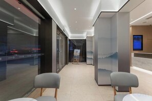 A hotel lobby with a reception desk, a digital screen, and two grey chairs. - Yilong Anyun Hotel (Rudong Chahe Middle School) (Rudong)