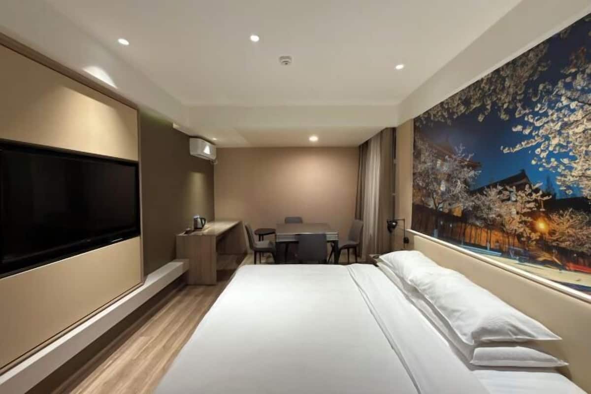 A hotel room with a large bed, a desk with a chair, a television, and a painting on the wall.
