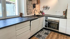 A modern kitchen with a stone accent wall, a built-in oven, and a black and white patterned rug. - delle Maschere by Interhome (Valli del Natisone)