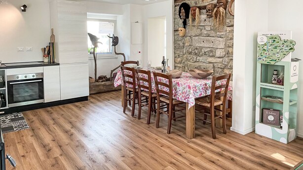A modern kitchen with a dining area, wooden flooring, and a stone wall with masks. - delle Maschere by Interhome (Valli del Natisone)