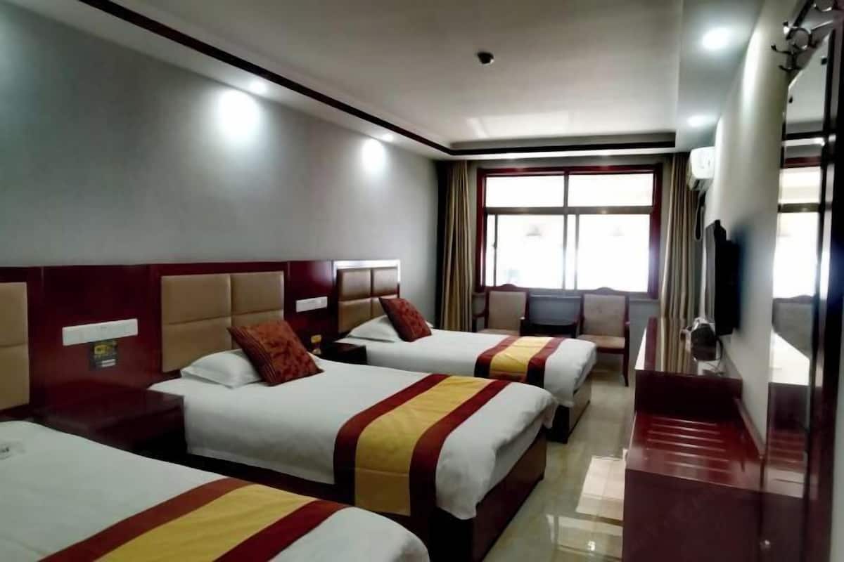 A hotel room with three beds, a television, and a window with curtains.