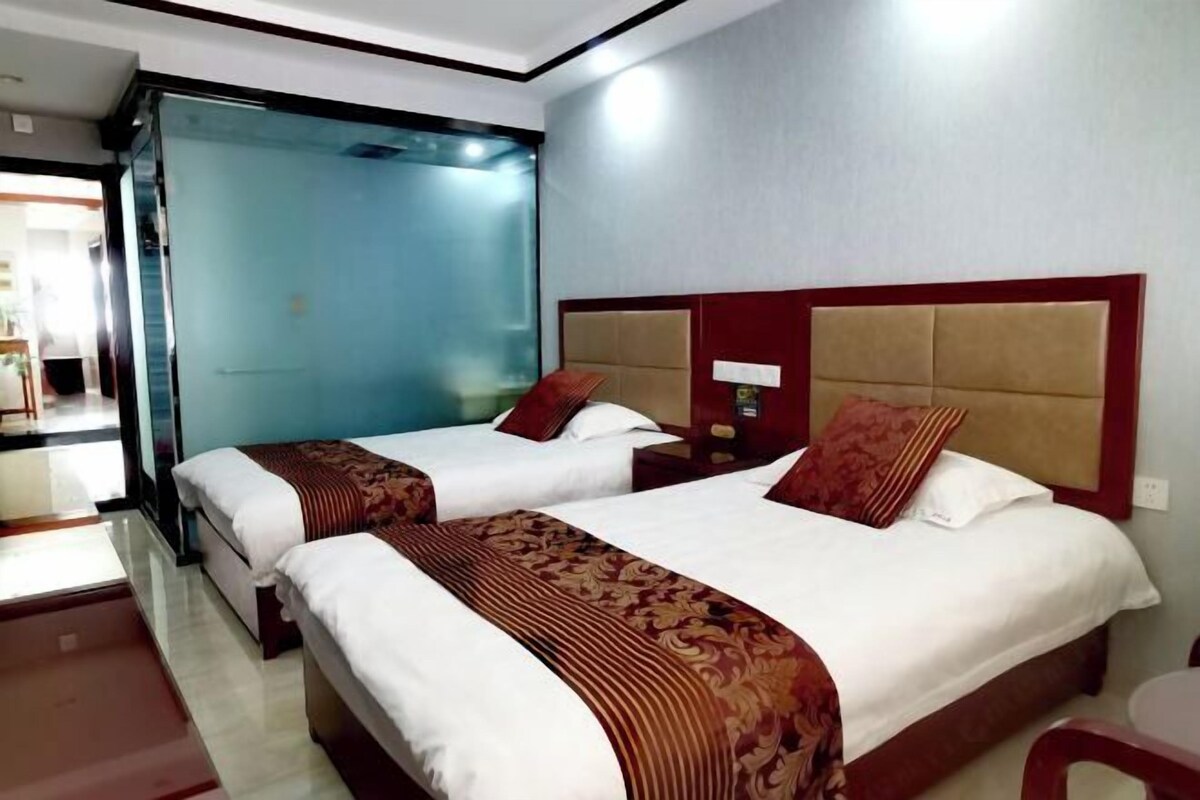 A hotel room with two beds, a glass partition, and a view of the outside.