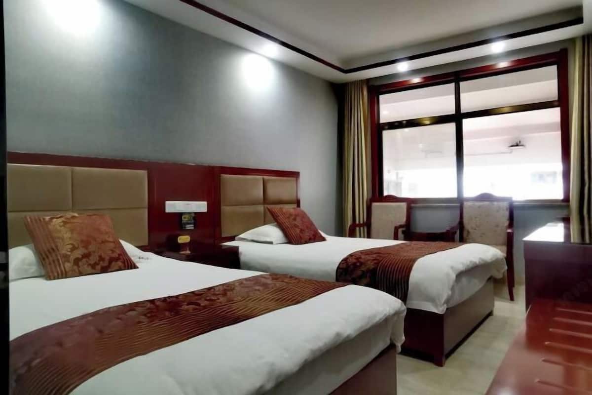 A hotel room with two beds, a large window with curtains, a desk, and a chair.