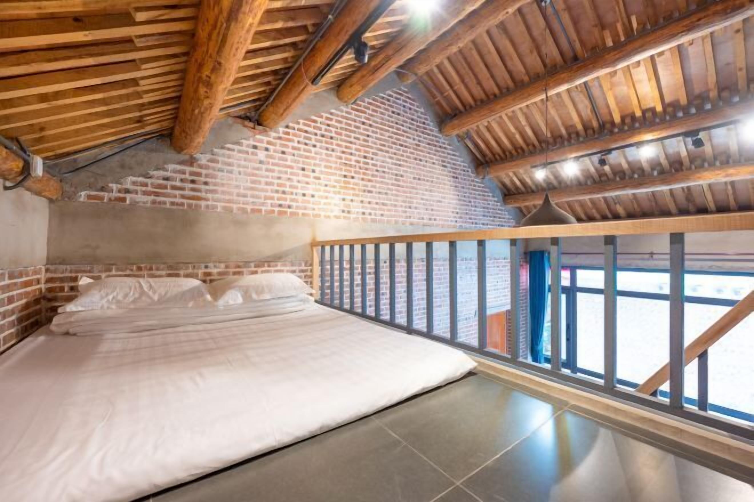 Ein Schlafzimmer mit Backsteinwand, Holzbalkendecke, einem Bett und Blick durch große Fenster.