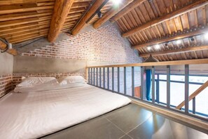 A bedroom with a brick wall, wooden ceiling beams, a bed, and a view through large windows. - Mutianyu Great Wall Country Park Homestay (Beijing)