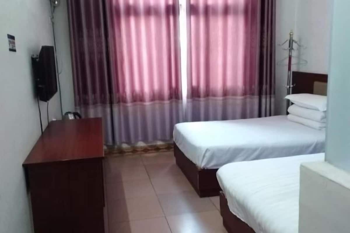 A hotel room with two beds, a wooden desk, a TV, and a wardrobe.