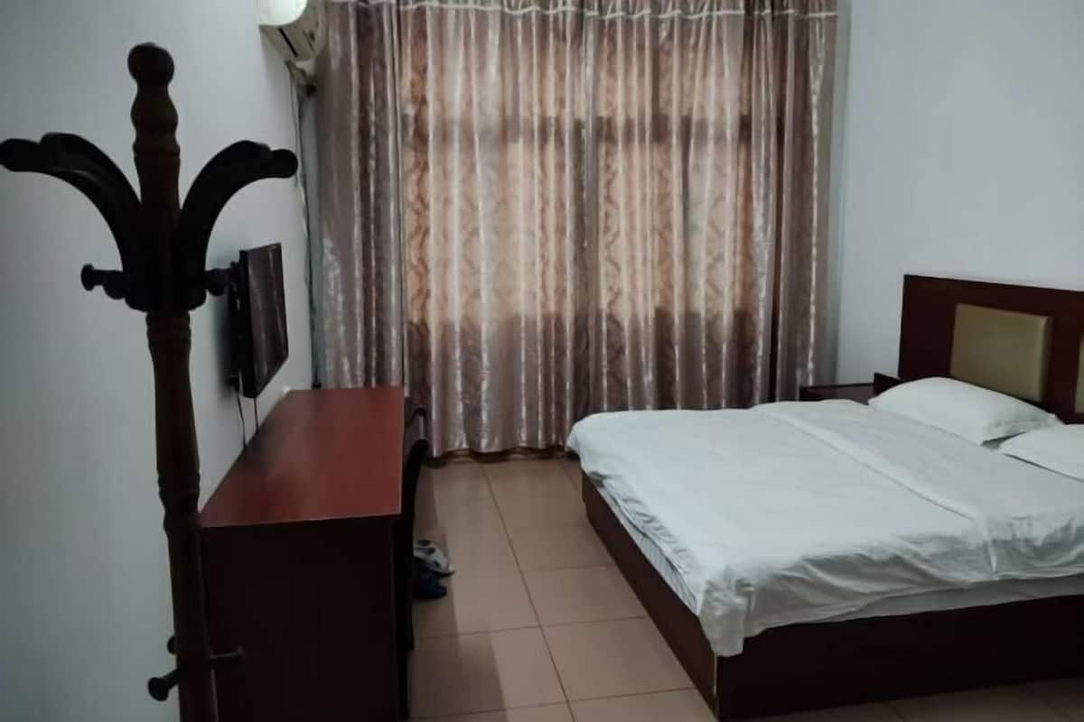 A bedroom with a bed, a wooden nightstand, a TV mounted on the wall, and a window with curtains.