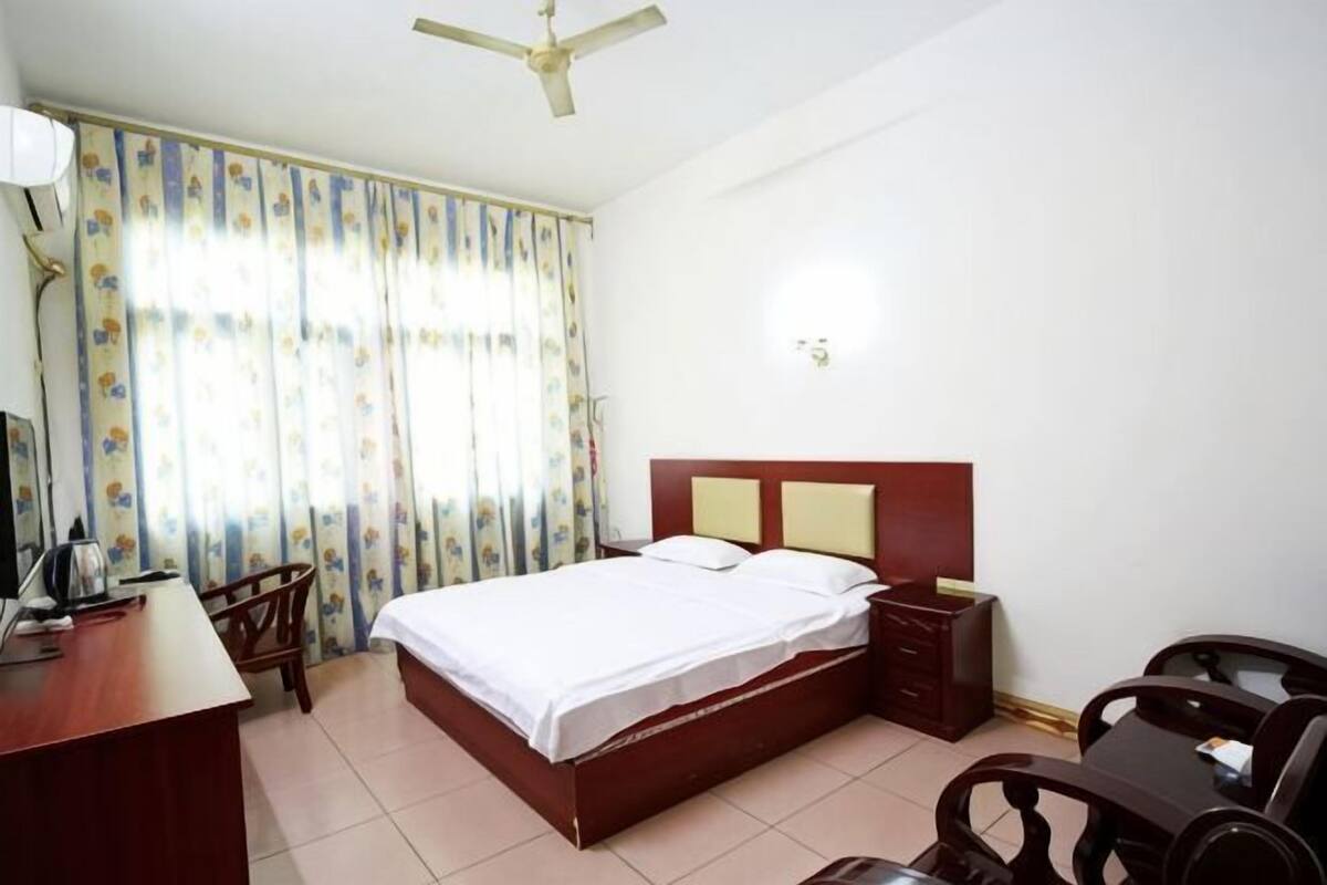 A hotel room with a bed, desk, chair, and a ceiling fan.