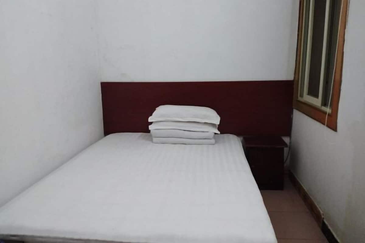 A small, single-bed room with a white mattress and a red headboard.