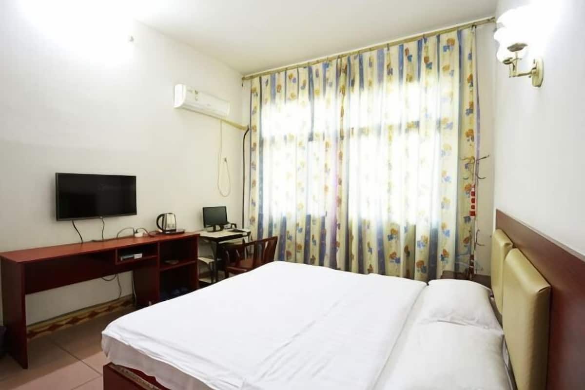 A hotel room with a bed, desk, chair, television, and curtains.