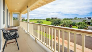 Un balcón techado con dos sillas y una mesa, con vista a una zona residencial con casas y vegetación.