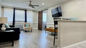 Una sala moderna con un sofá, un sillón y un televisor sobre un mueble bajo.