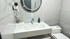 Ein Badezimmer mit einem weißen Waschbecken, einem runden Spiegel, einer Duschbrause und einer Toilette.