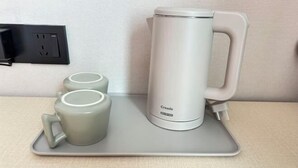 Ein grauer Tablett mit einem weißen Wasserkocher und zwei grauen Tassen auf einem Tisch.