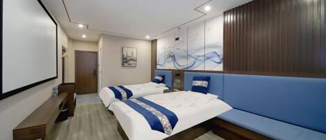 Habitación de hotel con dos camas, un sofá azul, un banco de madera y una obra de arte colgada en la pared.