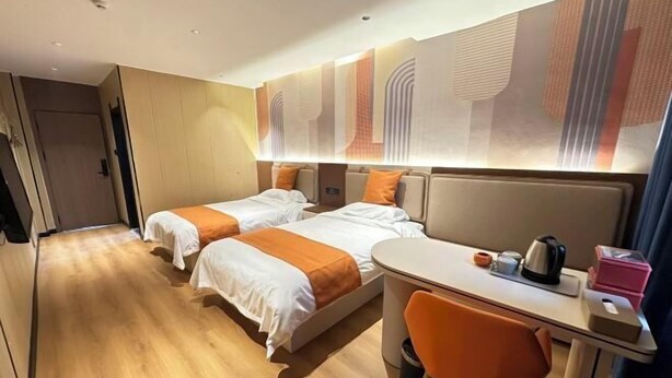 Ein Hotelzimmer mit zwei Betten, einem Schreibtisch mit Stuhl, einem Wasserkocher und einem Mülleimer.