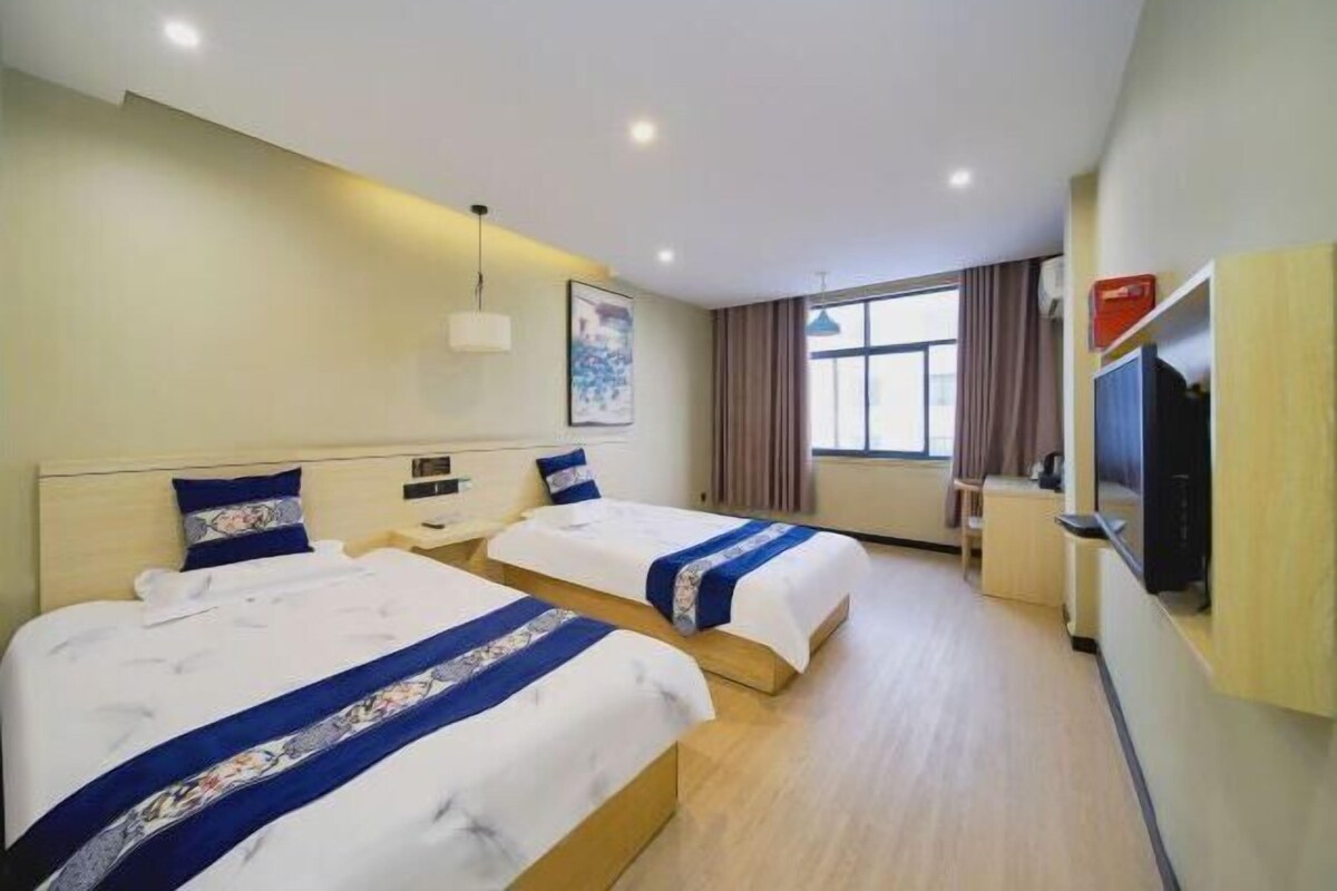 A hotel room with two beds, a TV, a desk, and a window with curtains.