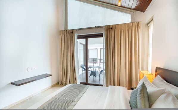A hotel room with a bed, a small table, and a view of the balcony.