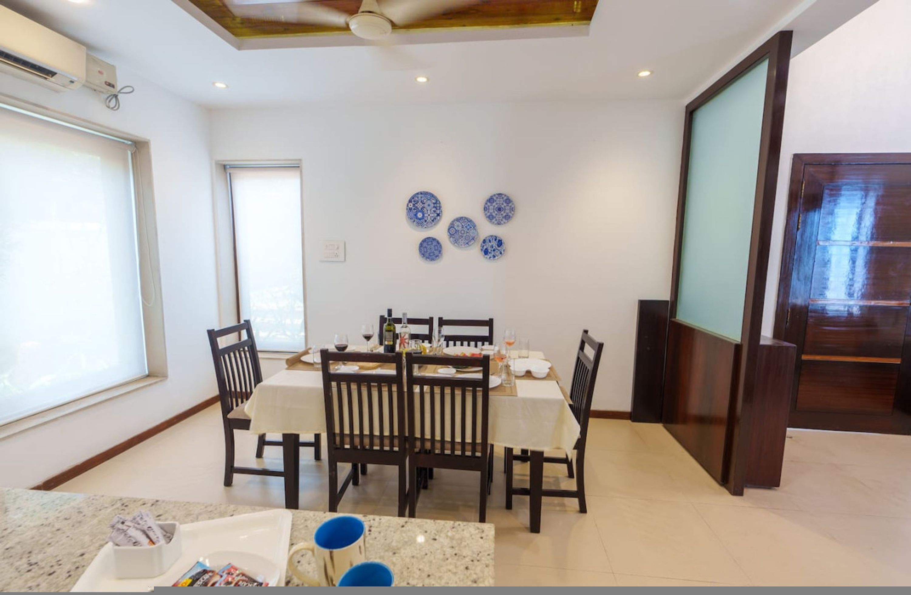 Un comedor con una mesa dispuesta para cuatro personas, rodeada de sillas y una pared decorativa con platos azules.