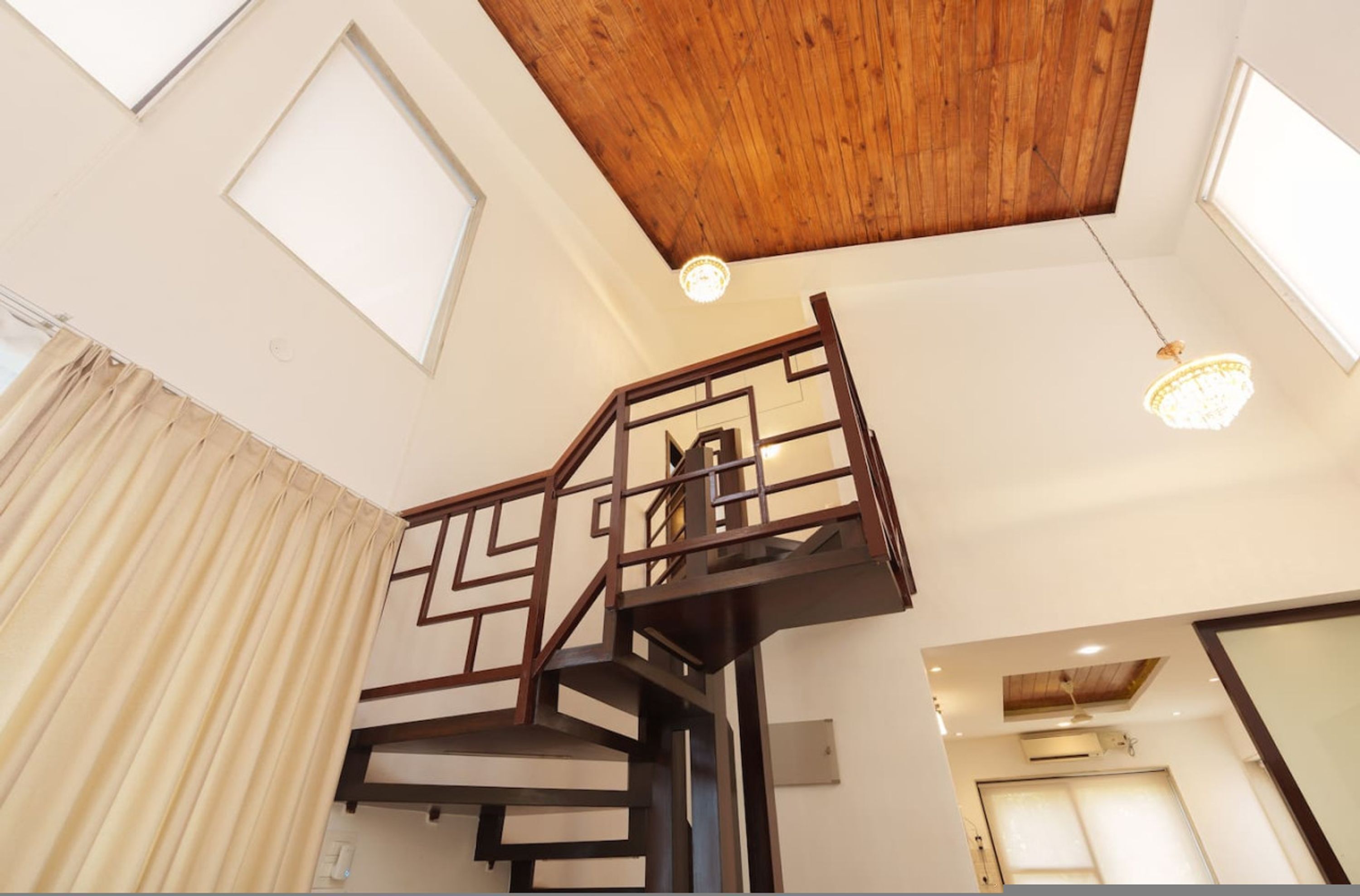 A modern interior with a wooden ceiling, a geometric staircase, and a chandelier.