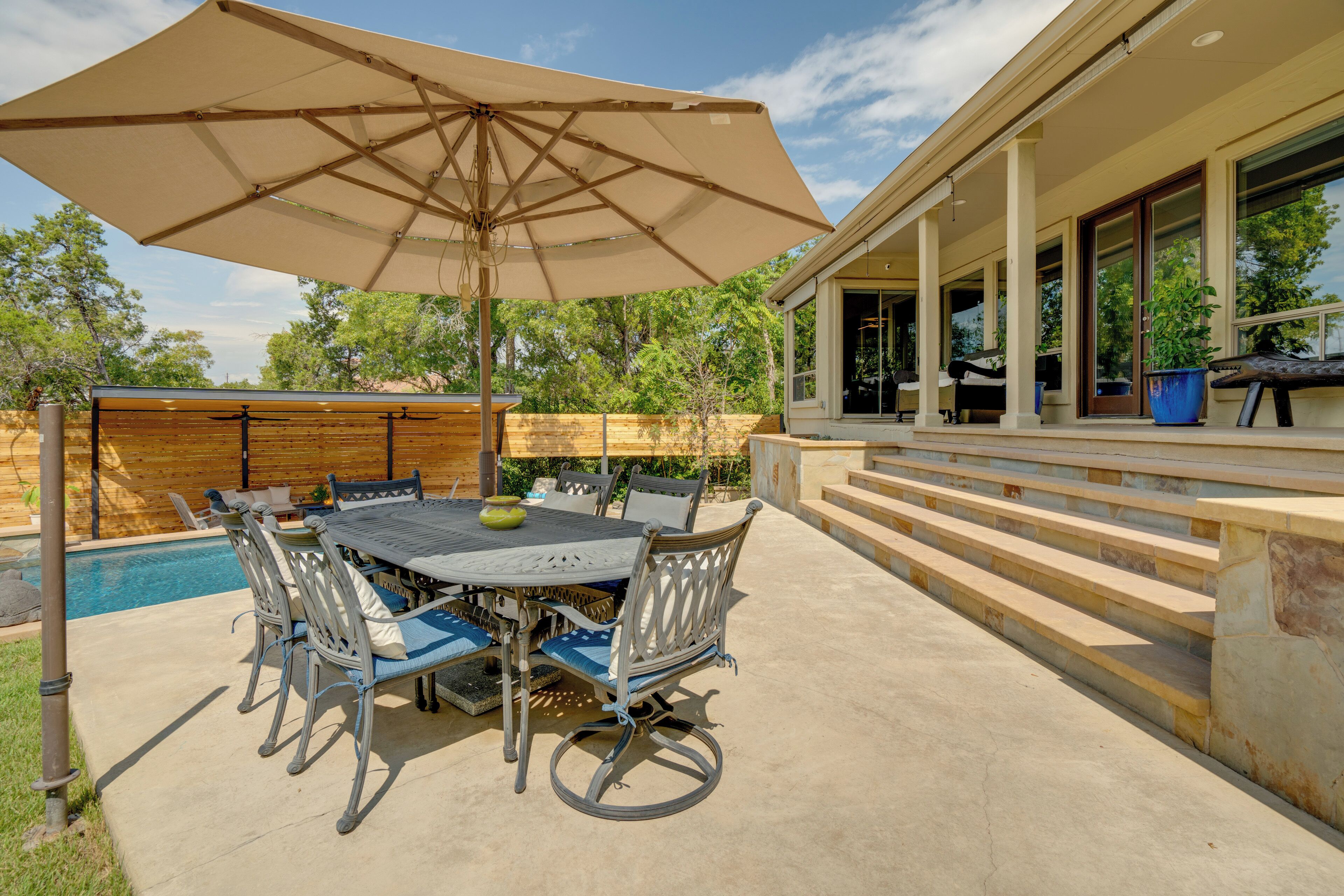 Un patio al aire libre con una mesa y sillas, una sombrilla grande y una piscina.