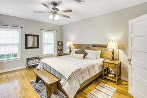 Un dormitorio con cama, mesitas de noche, un banco, ventilador de techo y una puerta.