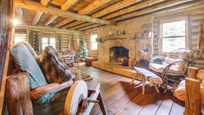 Ein rustikales Blockhaus-Interieur mit Kamin aus Stein, Holzmöbeln und einem Weihnachtsbaum.