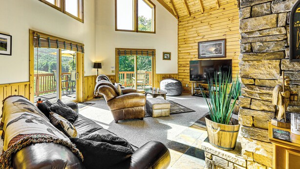 A spacious living room with leather sofas, a stone accent wall, a flat-screen TV, and large windows. - Deck & Mtn Views: Log Cabin By Snowshoe Mountain! (Valley Head)