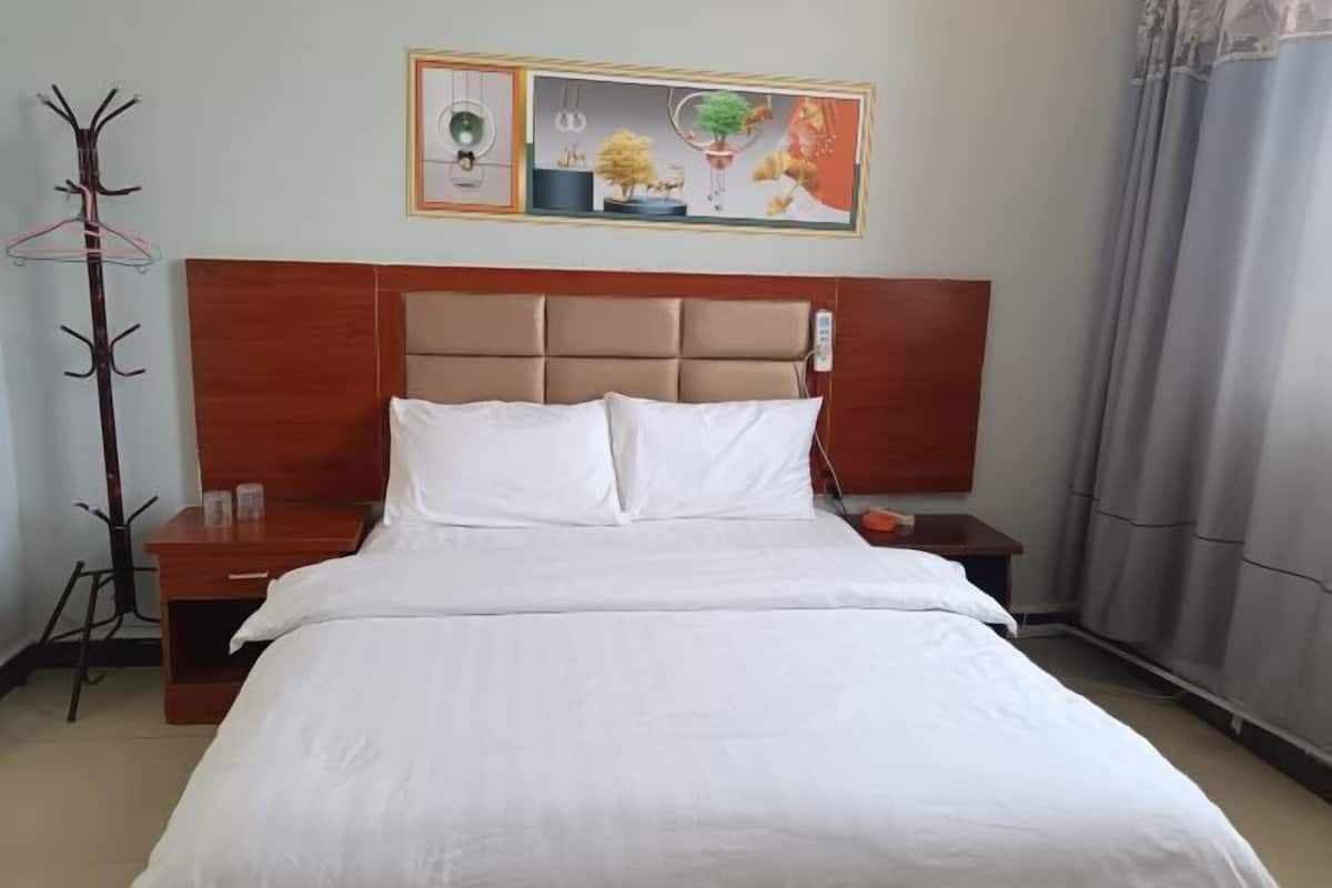 A hotel room with a bed, a nightstand, a coat rack, and a painting on the wall.