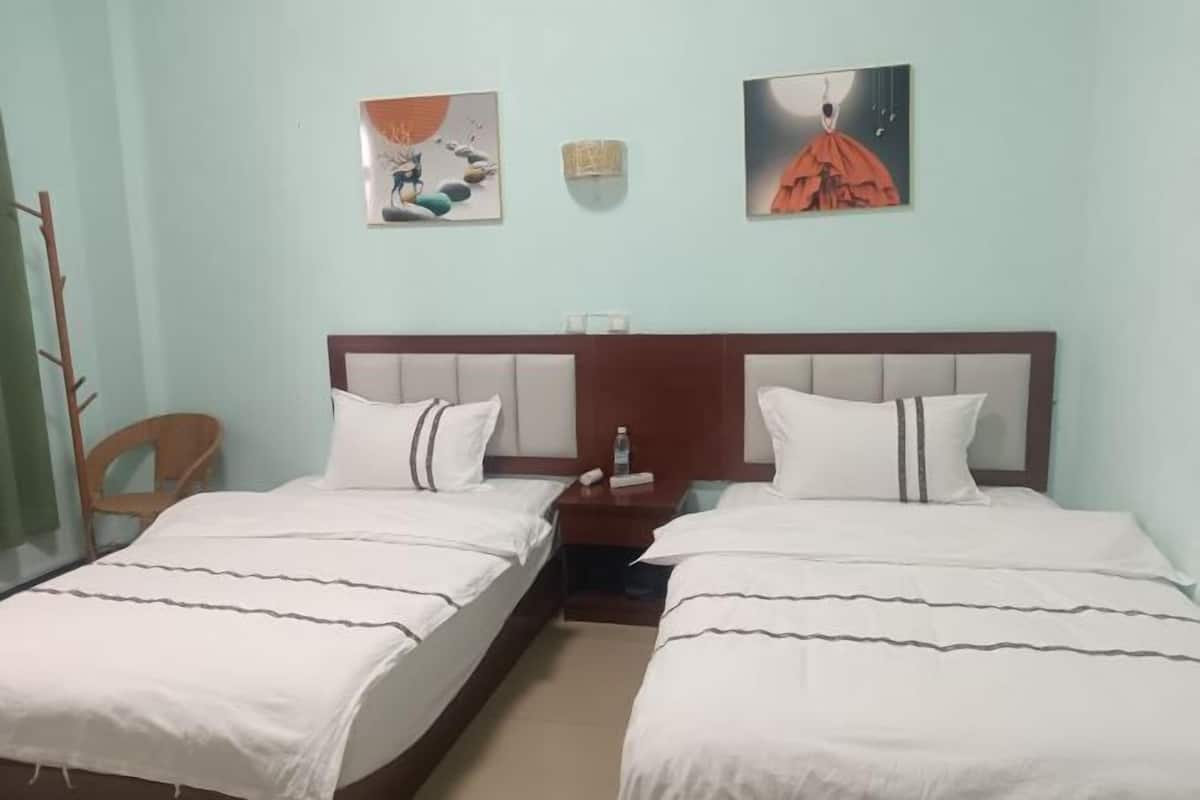 A hotel room with two beds, a nightstand, a chair, and two wall-mounted artworks.