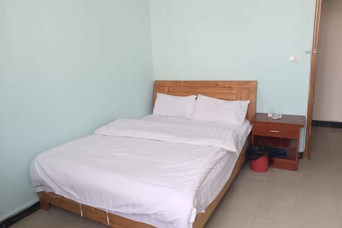 A single bed with a wooden headboard, a small bedside table, and a red trash bin.