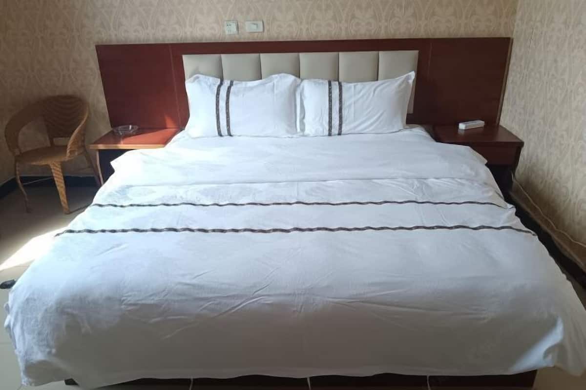 A hotel room with a large bed, a wooden headboard, and a nightstand with a remote control.