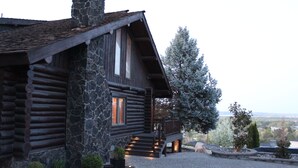 Una cabaña de troncos con chimenea de piedra, un porche de madera y un camino de entrada de grava.