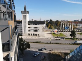 A modern building with a prominent tower, a large open plaza, and a clear sky.